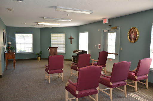 A serene interior space featuring a few chairs arranged around a small podium, with a cross on the wall.