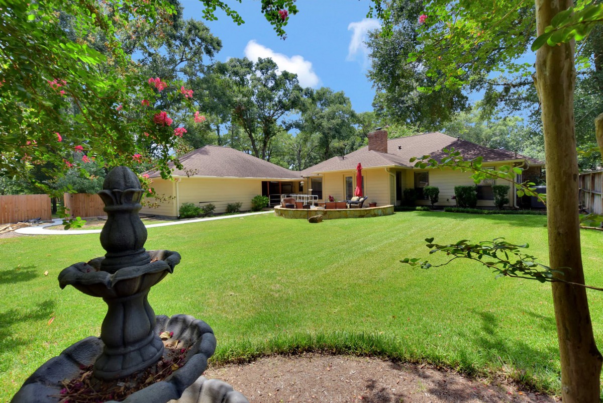 A spacious backyard with a well-maintained lawn and garden, featuring a patio area surrounded by trees.