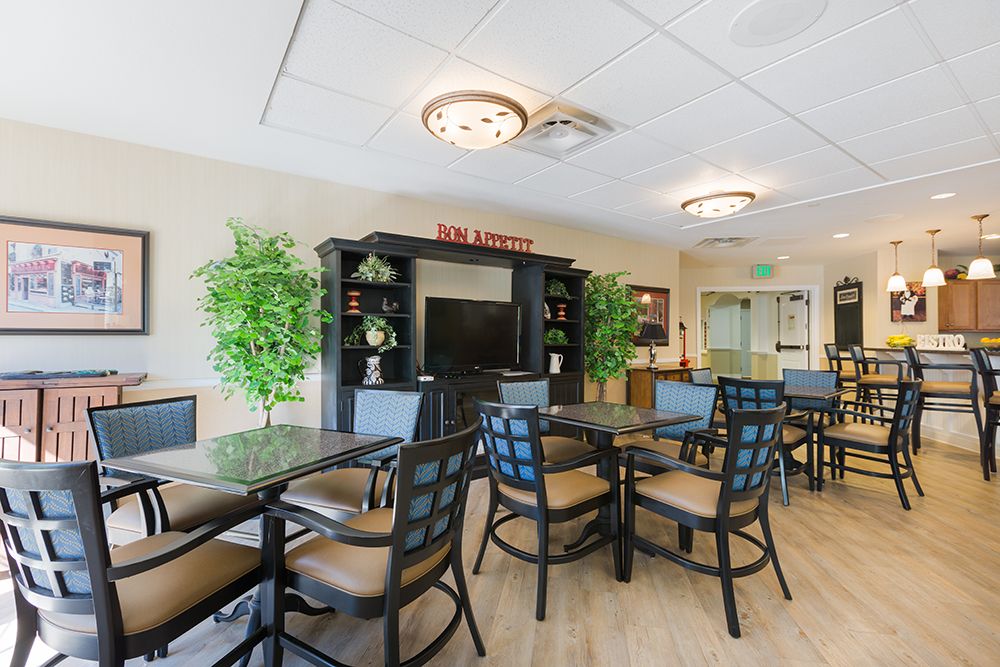 A well-lit seating area with tables, chairs, and a TV entertainment center.