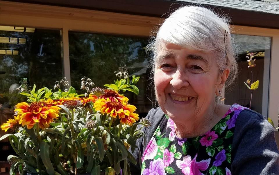 An elderly woman smiling while holding a bouquet of flowers in a garden.