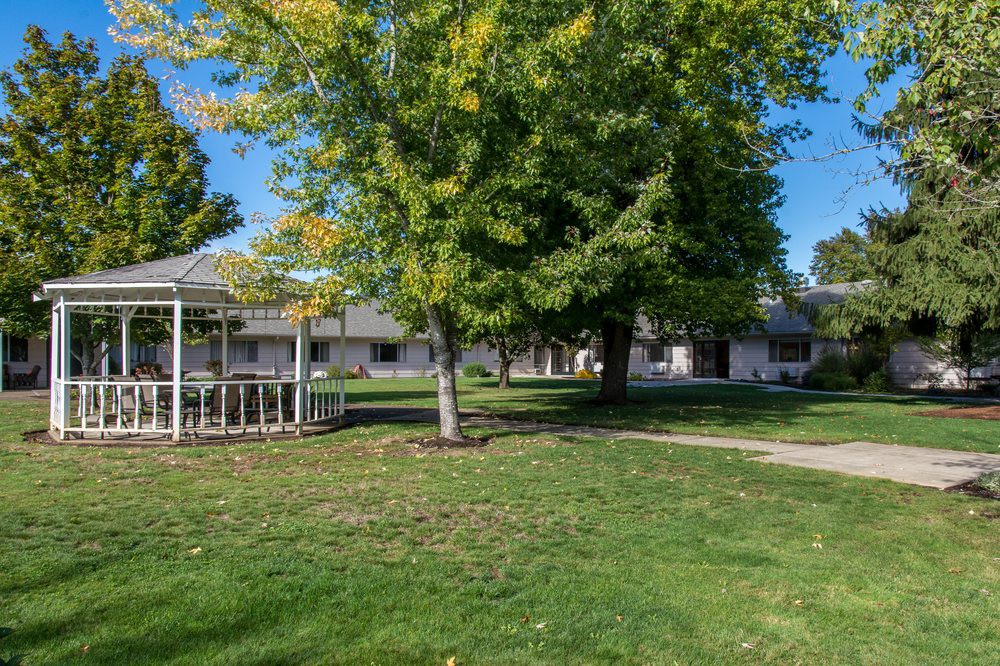 A tranquil outdoor scene featuring a gazebo, lush green grass, and trees under a clear blue sky.