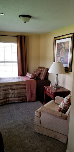 A cozy and well-decorated corner of a bedroom featuring a bed with decorative pillows, a lamp on a nightstand, and artwork on the wall.