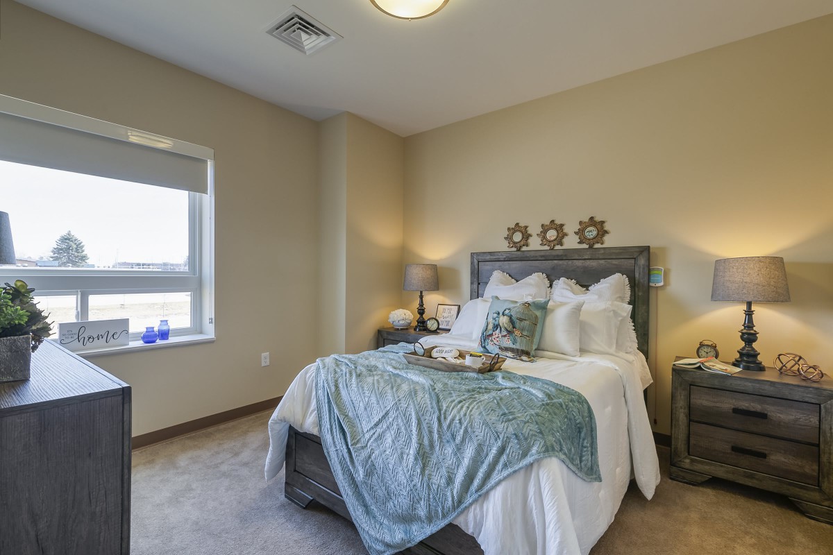 A cozy bedroom with a neatly made bed, featuring blue blankets and decorative pillows, flanked by nightstands and lamps.