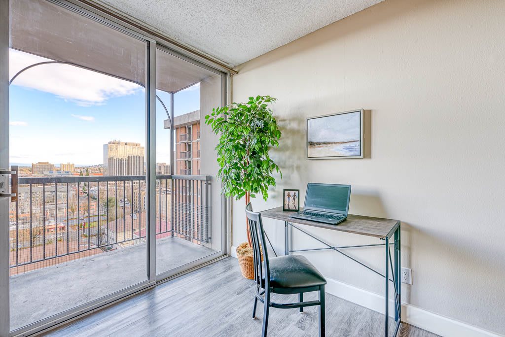 A cozy home office with a desk and laptop, adjacent to a balcony offering ample natural light.