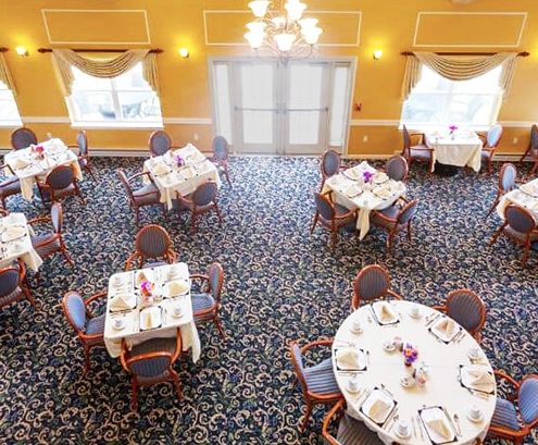 A spacious and elegantly decorated dining room with round tables set for a formal occasion.