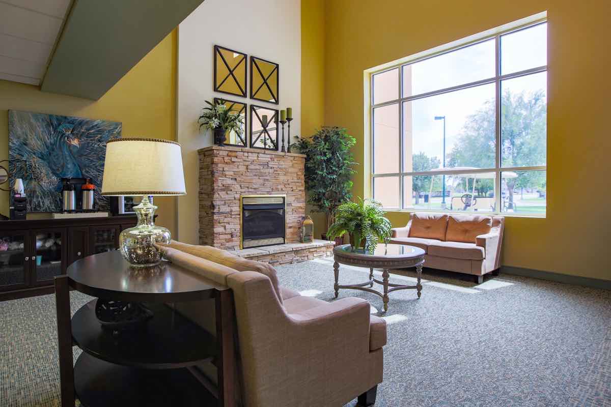 A cozy living room with a fireplace and large window, furnished with sofas, a table, plants, and a lamp.