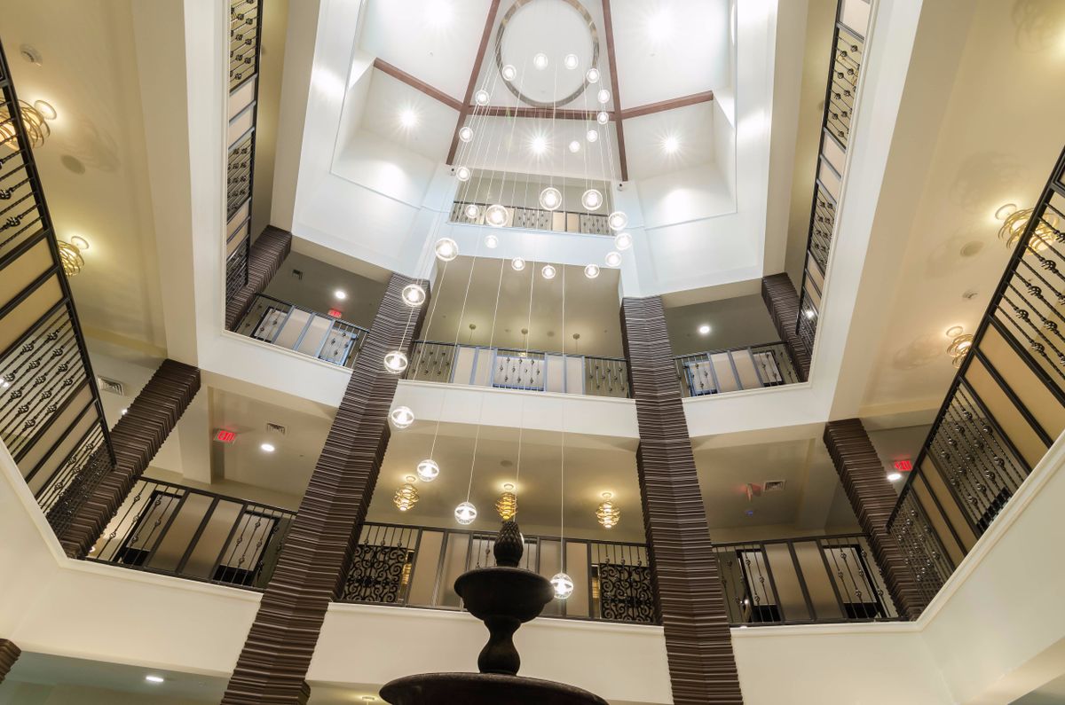 A modern atrium interior with multiple balconies, a central chandelier, and a fountain at the base.