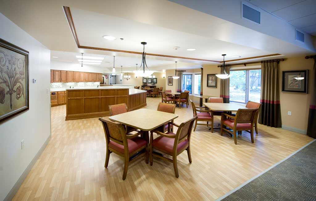 A spacious dining area with wooden tables and chairs, featuring a kitchen in the background.