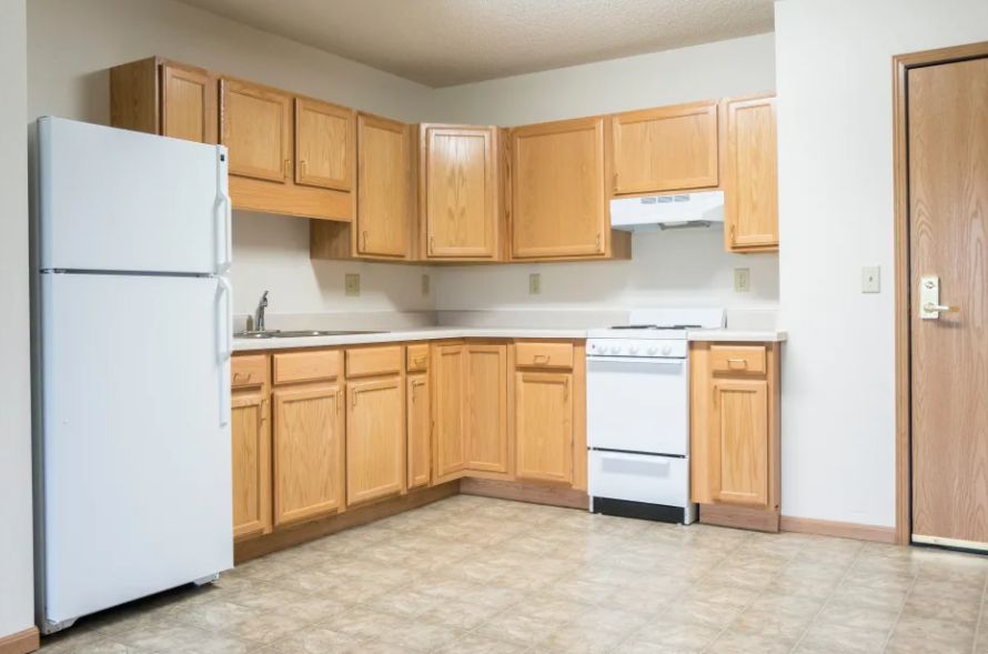 An empty apartment kitchen featuring wooden cabinets, a refrigerator, and a stove.