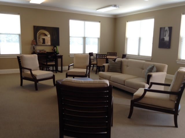 A cozy living room furnished with sofas and chairs, featuring ample natural light from the windows.