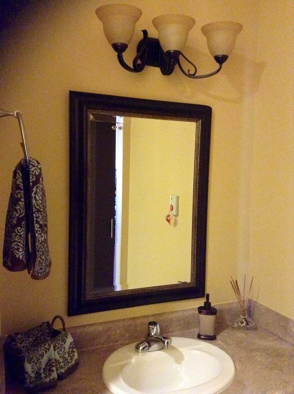 A bathroom with a mirror above the sink, featuring a towel hook and light fixture.