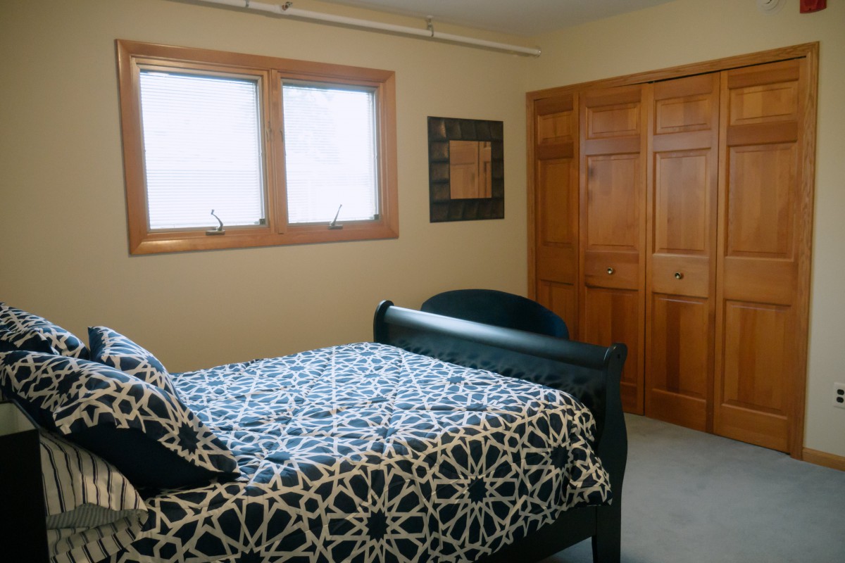 A cozy bedroom with a patterned bedspread, wooden closet, and natural light from the windows.