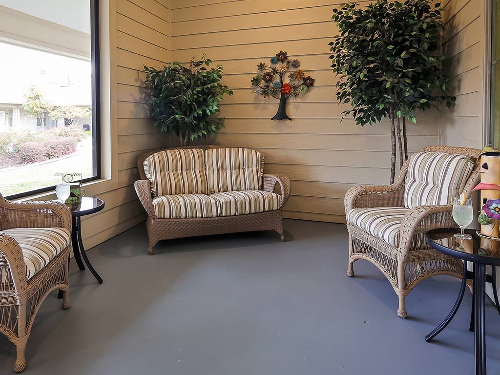 A cozy patio area featuring wicker furniture with striped cushions, surrounded by leafy plants and wall decor.