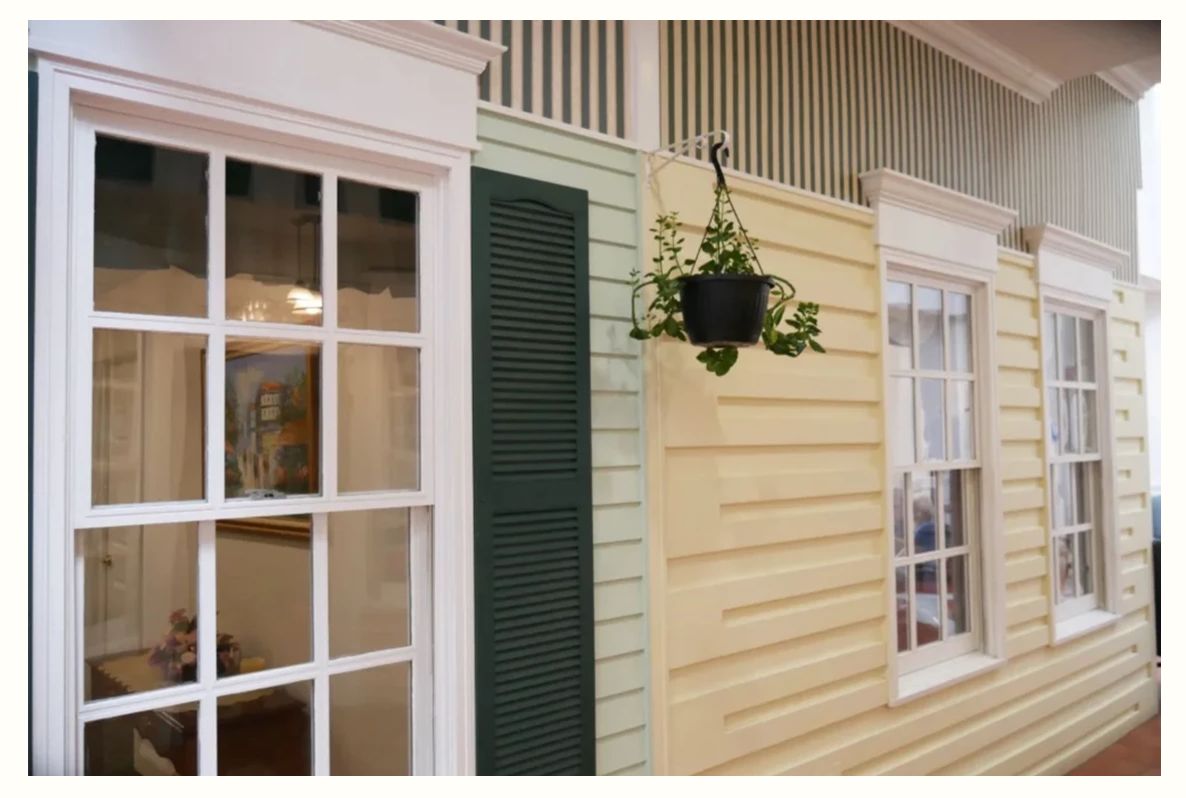 A hanging plant decorates the exterior of a house with large windows and shutters.
