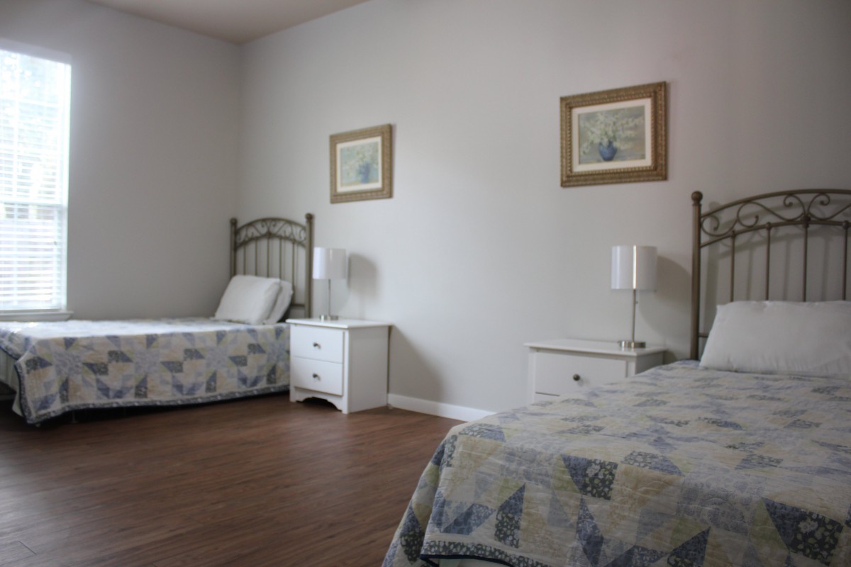 A minimalist bedroom with twin beds, each accompanied by a nightstand and lamp, decorated with framed pictures on the wall and a wooden floor.