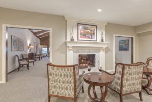 A cozy living room with a fireplace, two upholstered chairs, and a small wooden table set for two.