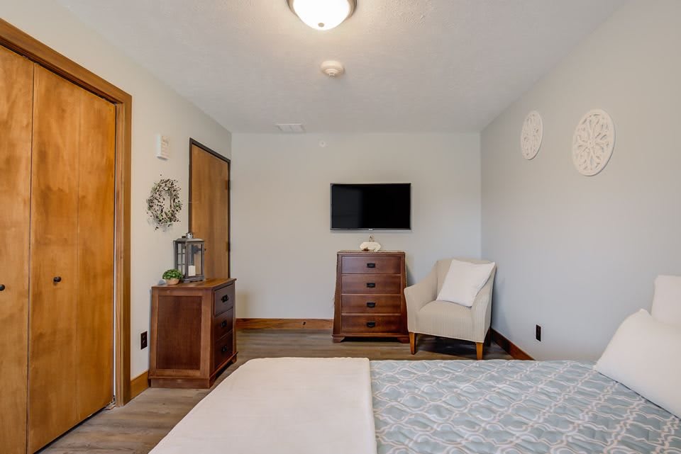A modern and minimalist bedroom with a mounted television, dresser, and comfortable chair.