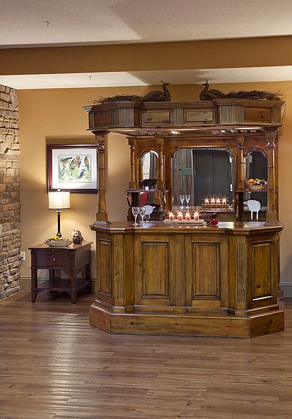 A vintage-style wooden home bar set against a warm-toned interior with a side table and lamp.