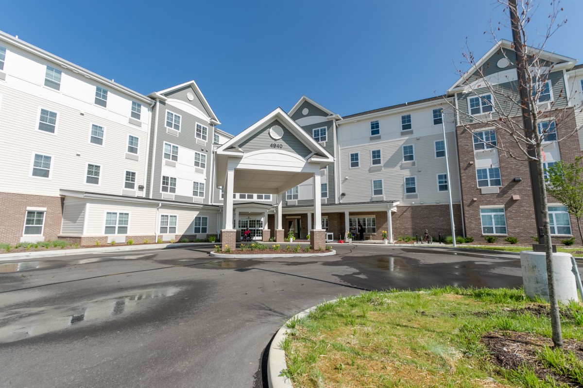 A large residential building with an entrance and parking area on a clear day.