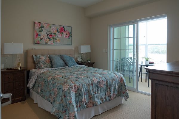 A cozy bedroom with a floral bedspread, artwork on the wall, and access to a balcony through sliding glass doors.