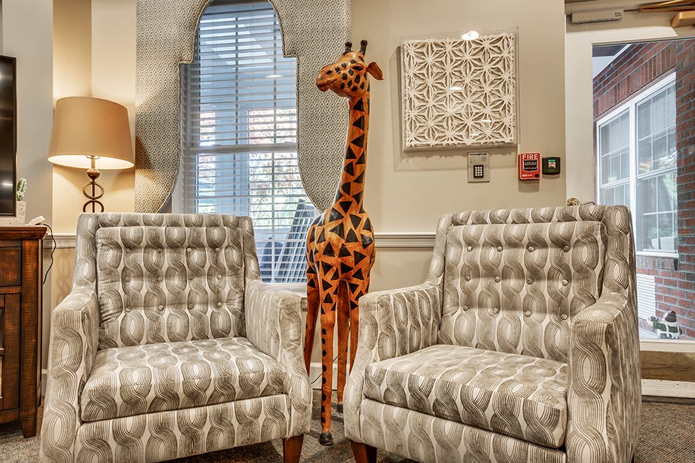 A plush giraffe stands between patterned armchairs in a cozy living room setting.