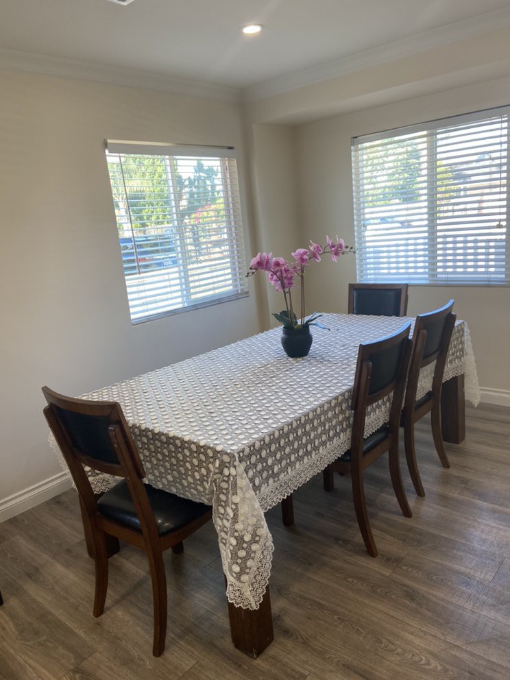A dining room with a table covered by a tablecloth, surrounded by chairs and decorated with an orchid in a flower vase.