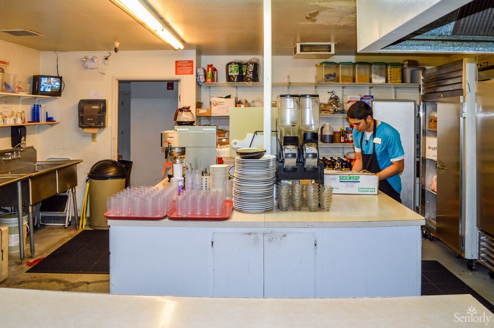 A worker in a restaurant kitchen preparing drinks and organizing dishes.