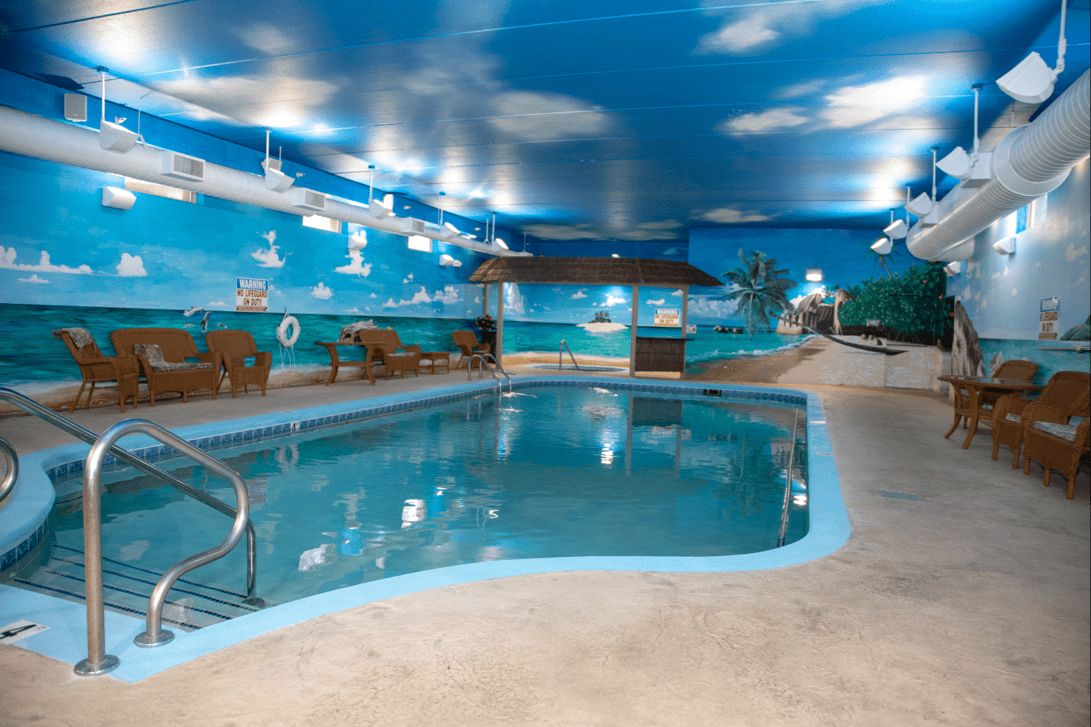 A vibrant indoor pool area with tropical-themed murals and cloud decorations on the ceiling.