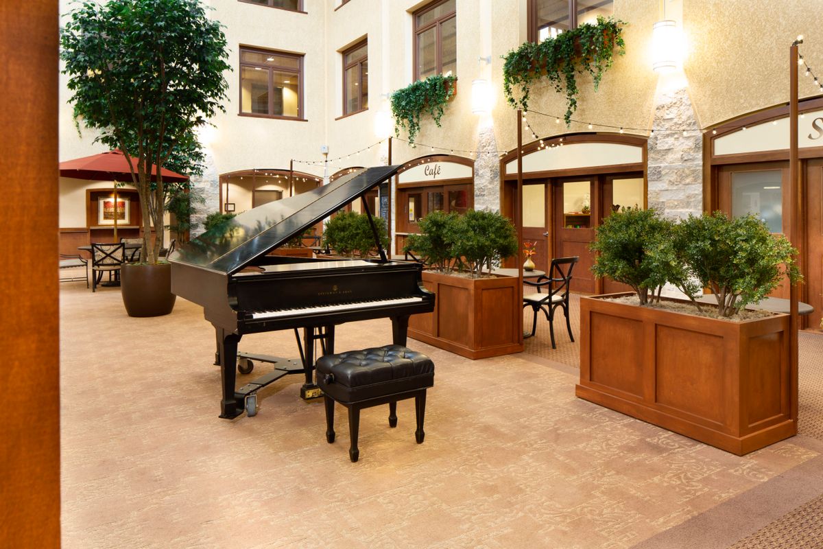 A spacious lobby featuring a grand piano and seating area surrounded by lush greenery.
