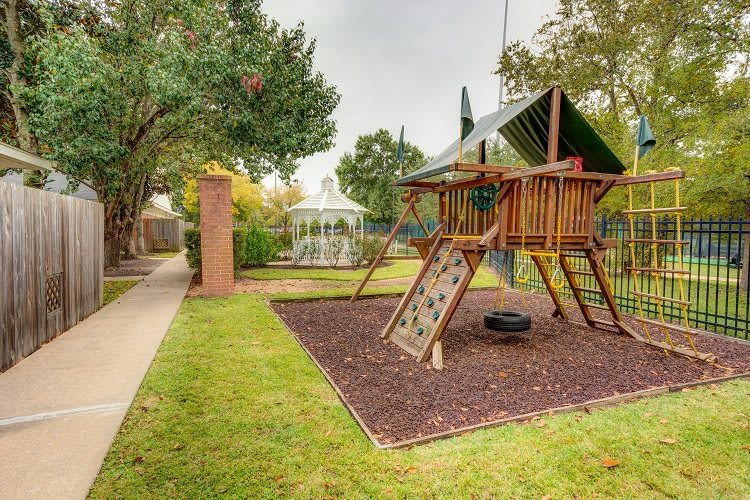 A children's playground with a swing set and slide, adjacent to a gazebo in a grassy outdoor park.
