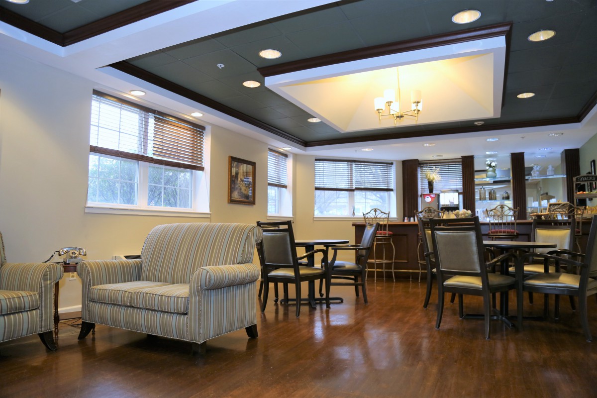 A cozy lounge area with comfortable seating and a chandelier, featuring wooden floors and large windows.