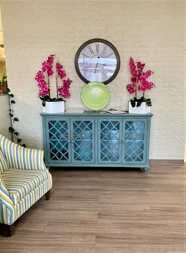 A beautifully decorated living space featuring a stylish sideboard adorned with vibrant flowers and a round mirror, complemented by a cozy striped chair.
