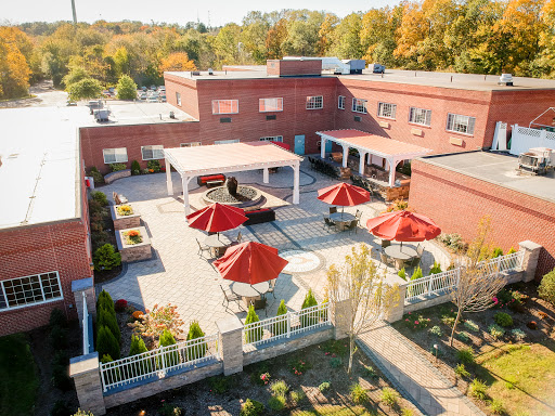 Aerial view of a modern building with a landscaped patio featuring red umbrellas, set against a backdrop of autumn foliage.