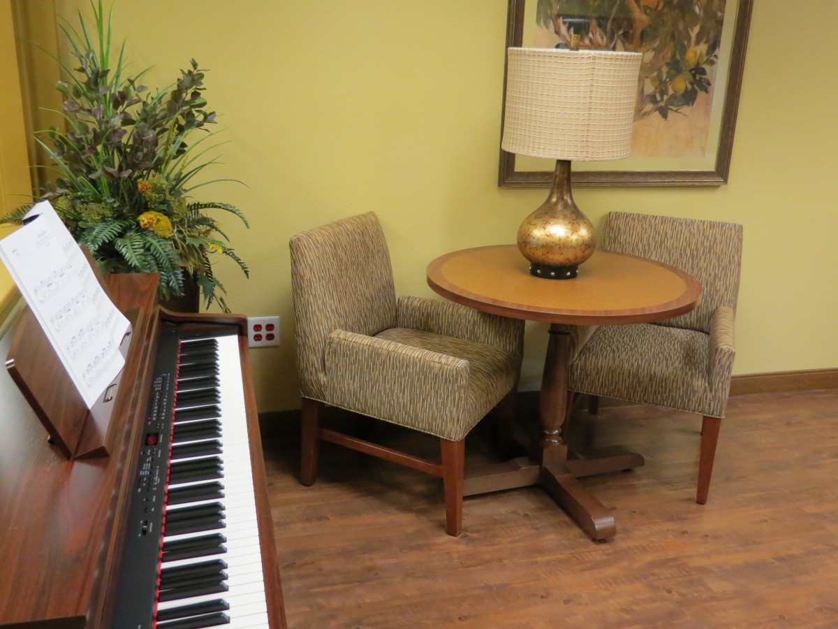 A cozy corner with a piano, small round table, two chairs, and a lamp.
