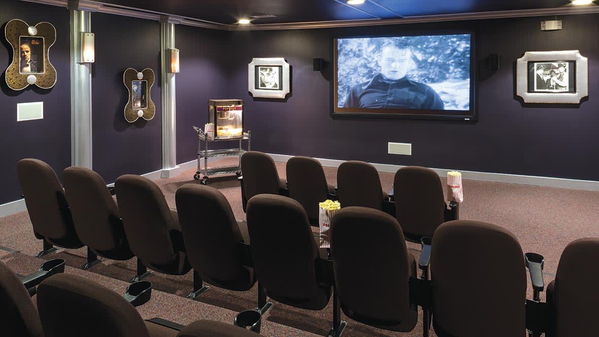 A cozy home theater setup with rows of seating and a large screen displaying a film.
