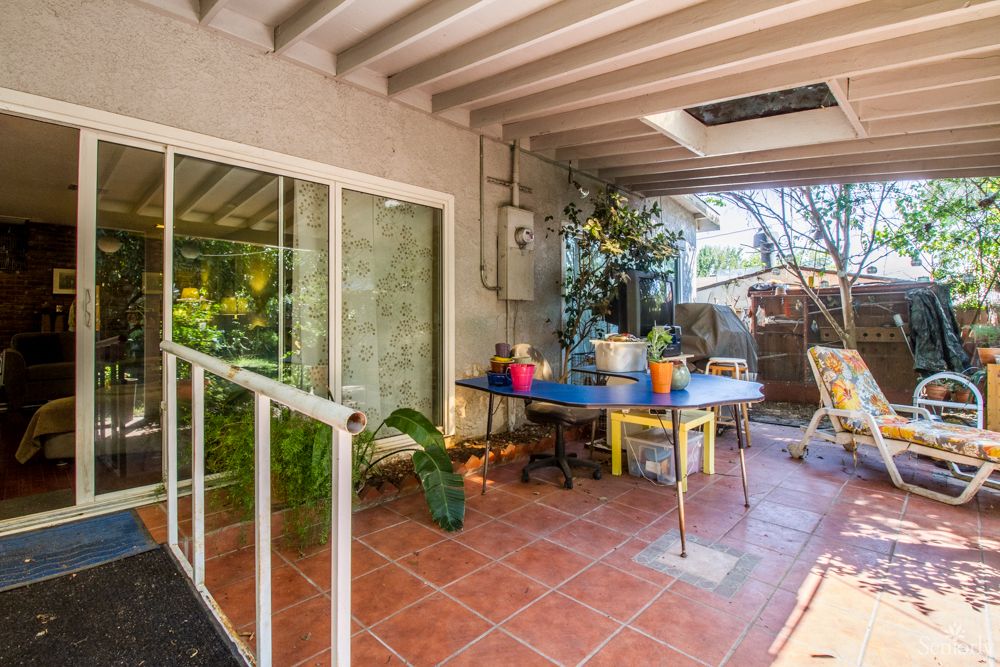 A cozy outdoor patio with a table and chairs, surrounded by plants and sunlight.