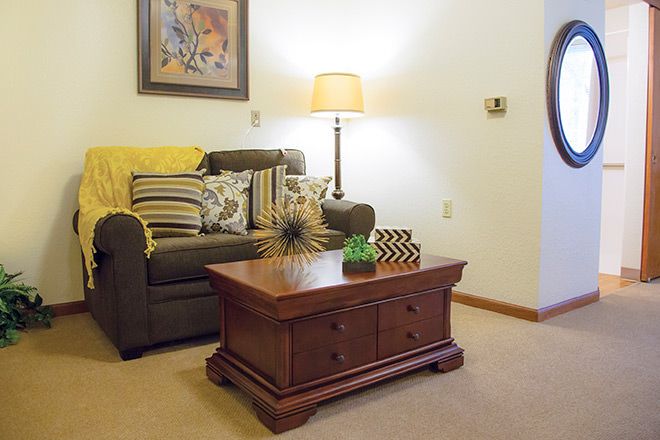A cozy living room with a sofa adorned with cushions, a wooden coffee table, and a standing lamp, complemented by wall art.