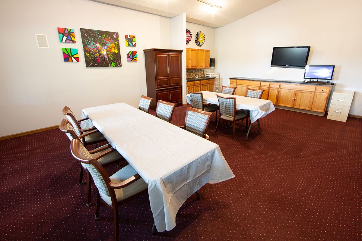 A well-equipped conference room featuring tables covered with white cloths, chairs, a television, artwork on the walls, and a carpeted floor.