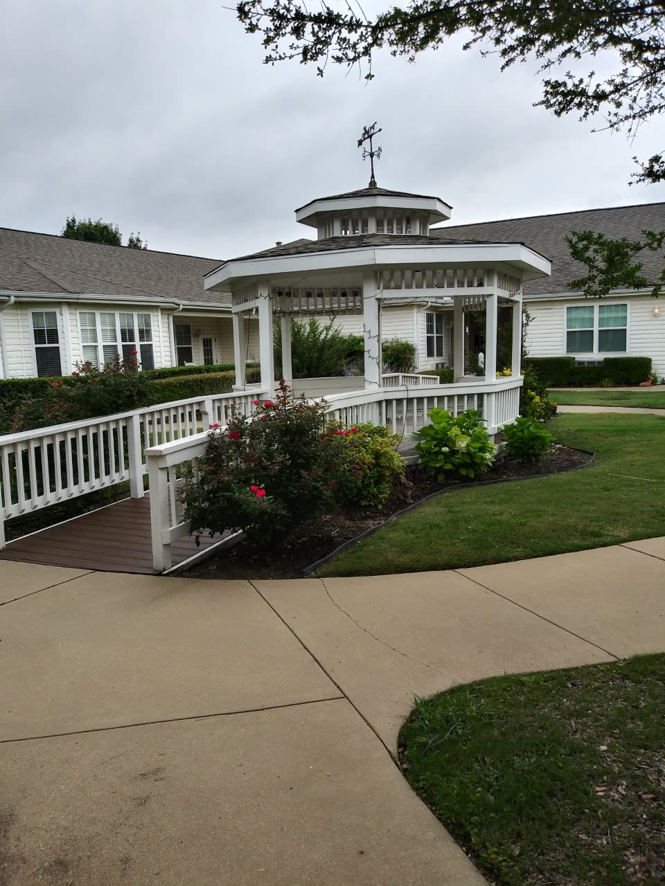 A charming gazebo surrounded by a garden with a paved pathway leading to it.