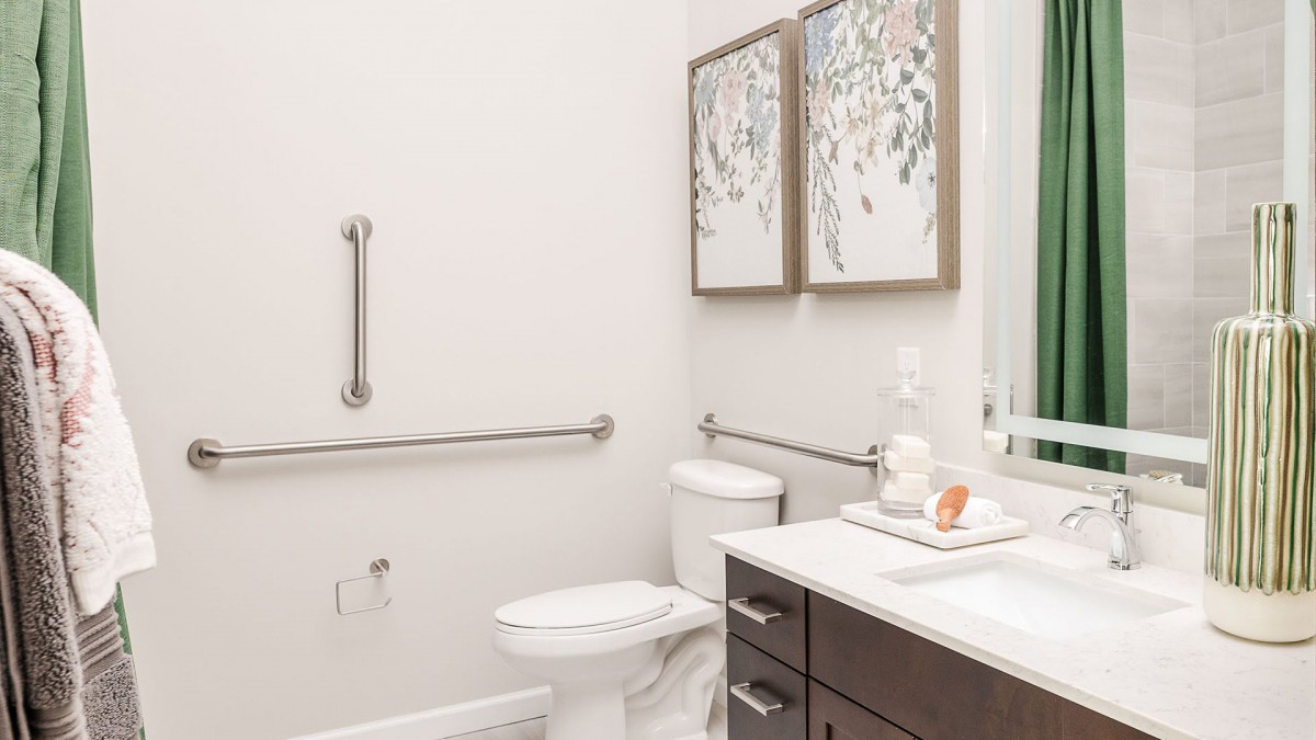 A modern bathroom with accessibility features, including handrails near the toilet and sleek decor.