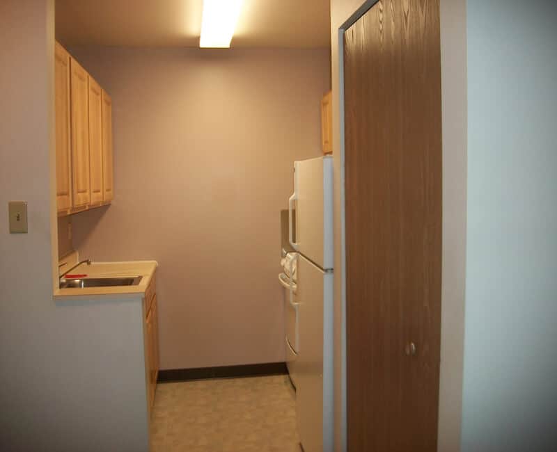 A small kitchen with wooden cabinets, a refrigerator, and a sink in an apartment.