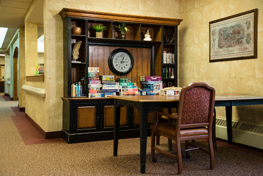 A cozy reading corner featuring a wooden shelf stocked with board games and a clock, accompanied by a table and chair.