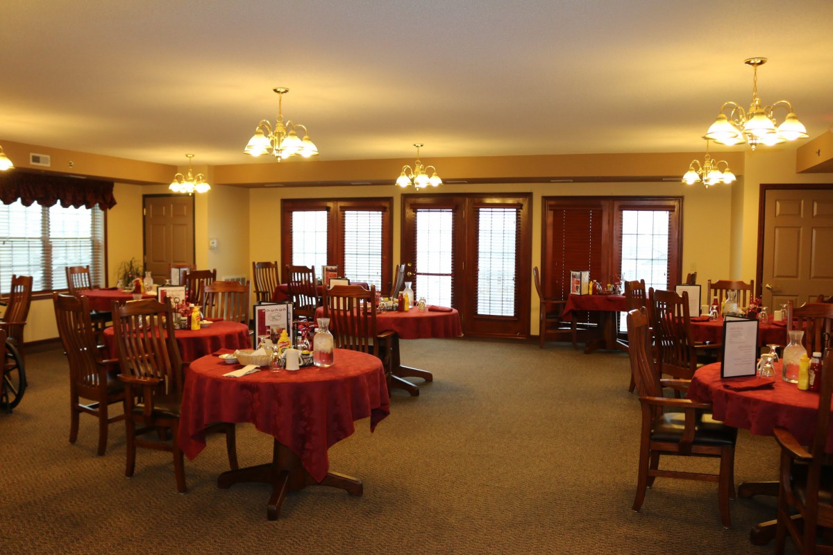 An empty dining room with tables and chairs set with red tablecloths.