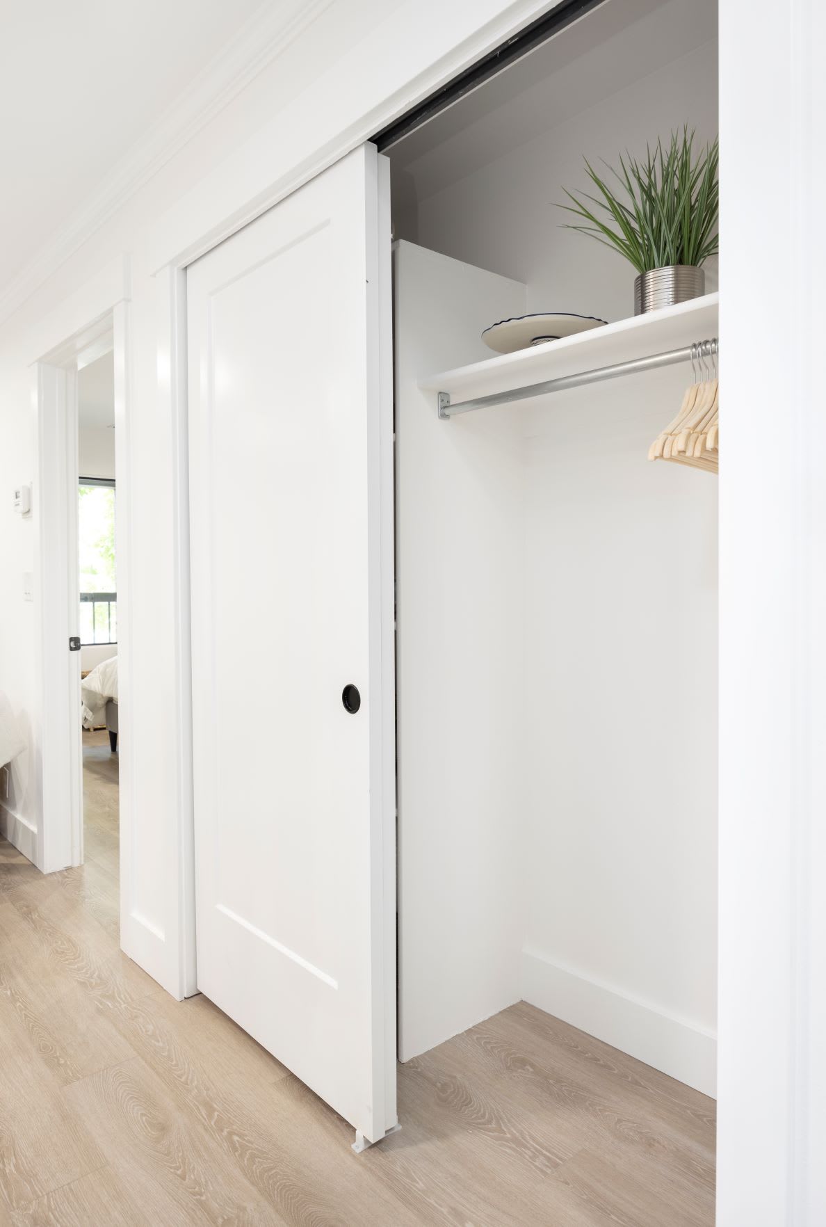 A minimalist white closet with an open sliding door and a hanging rod.