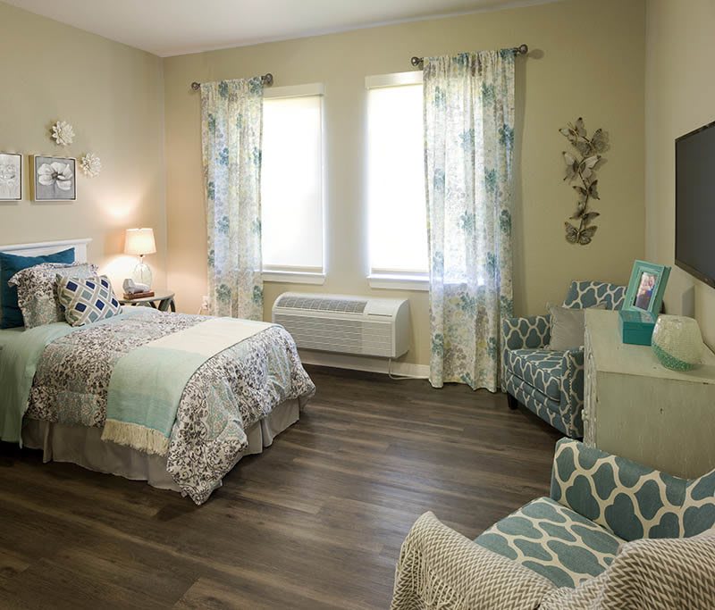 A cozy bedroom featuring stylish decor with a bed, chairs, and large windows allowing natural light.