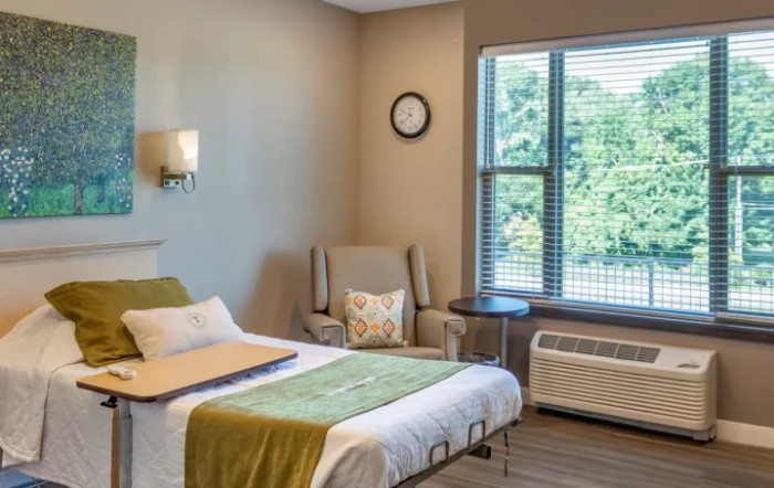 A cozy and minimalist bedroom with a single bed, armchair, and large window allowing natural light to fill the space.