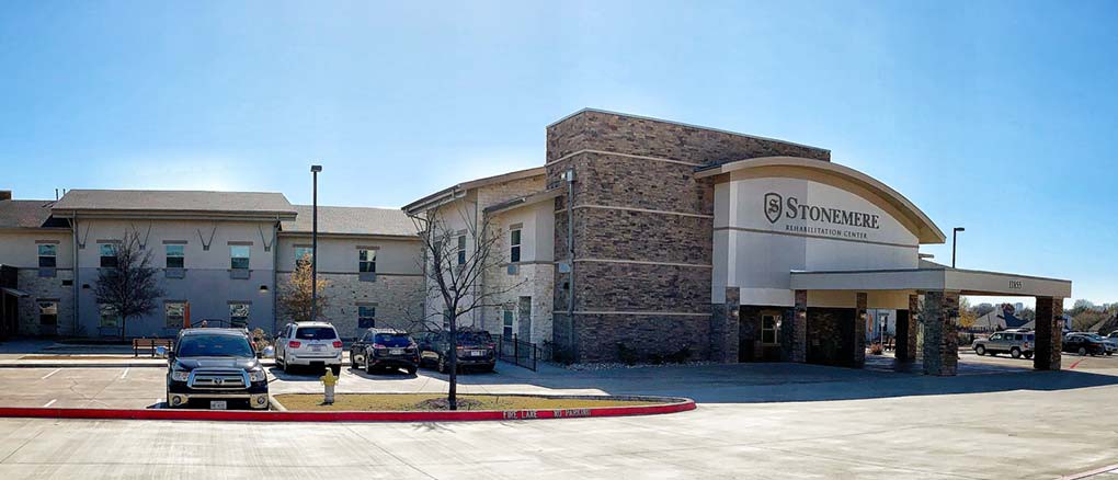 A commercial building with a parking lot and several cars parked in front of it on a clear day.