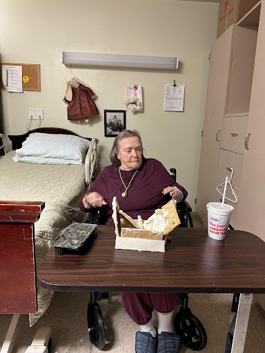 An elderly woman seated at a table in a nursing home, enjoying her meal.