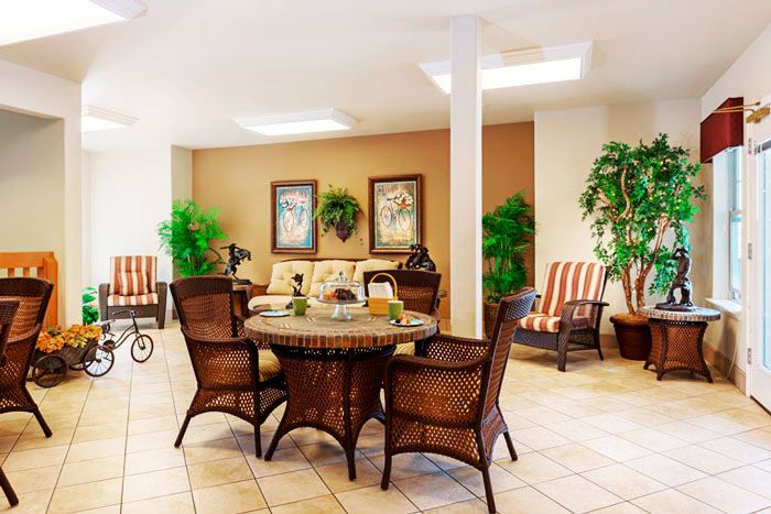 A cozy living room with wicker chairs and a table, decorated with plants and artwork.