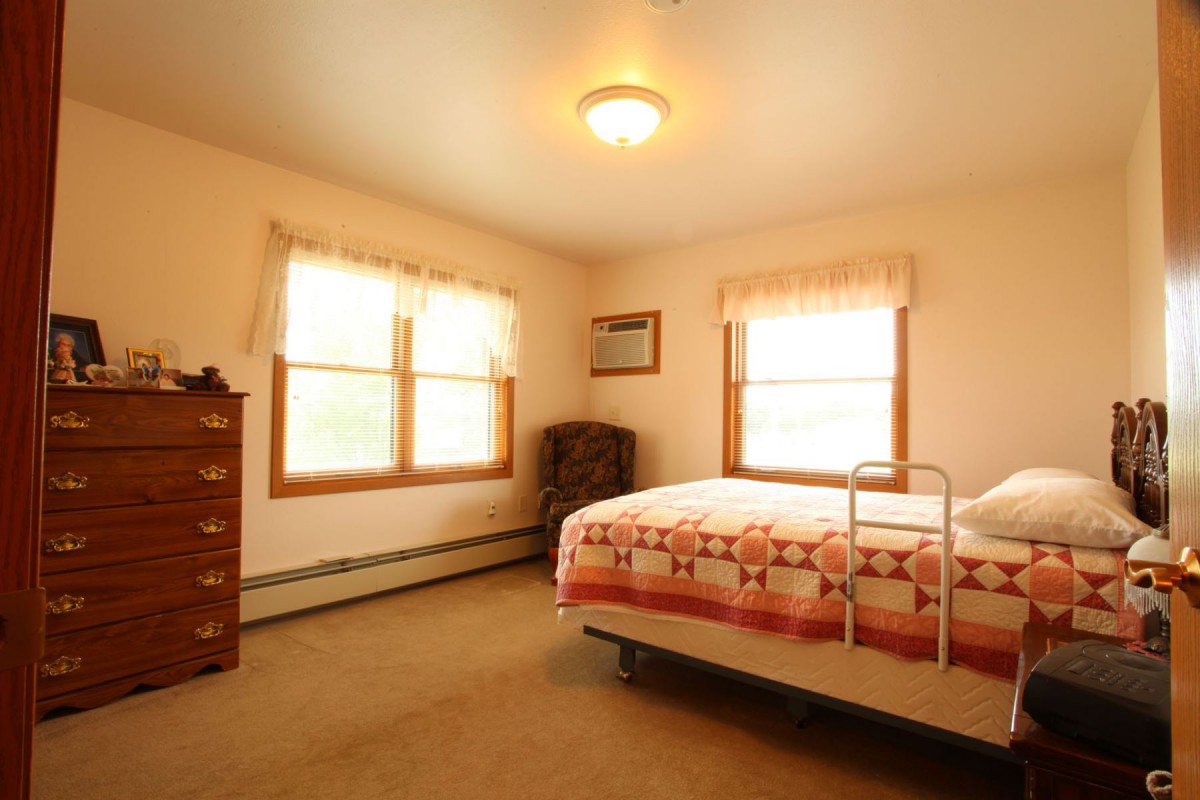 A cozy bedroom with a bed, dresser, and armchair by the window.